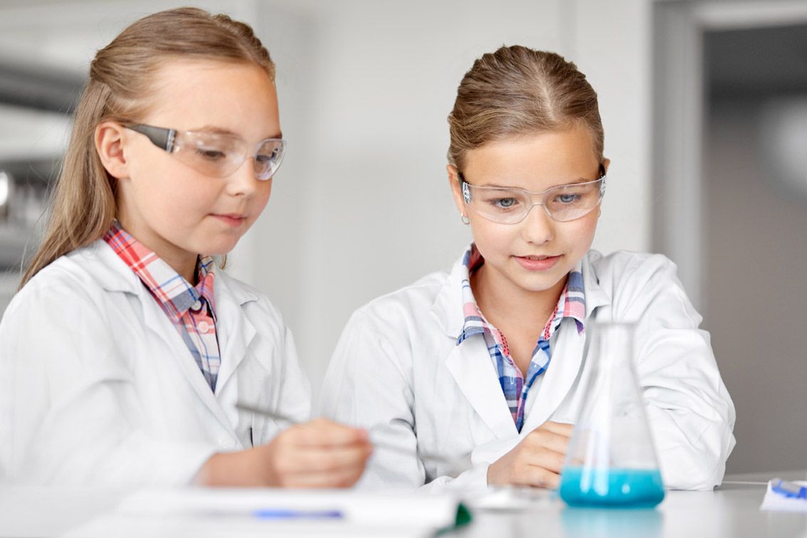 education, science and children concept - girls in goggles with test tube studying chemistry at school laboratory